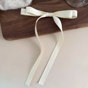 Detailed view of the off-white satin bow hair clip with long flowing ribbons on wood