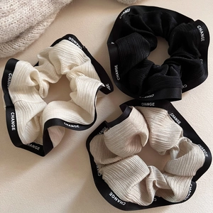 Close-up of three scrunchies with pleated texture and black ribbon edge with CHANGE text