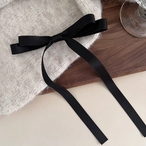 Oatmeal knitted hair clip with a long black satin ribbon bow on a wooden surface