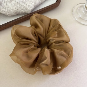 Gros plan d'un chouchou en tulle caramel orné de délicates perles blanches satinées