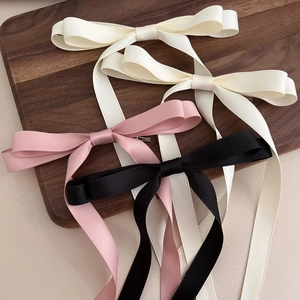 Macro shot of silk satin bow hair clips in beige, pink, and black on a wooden tray