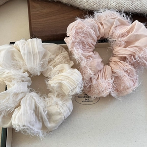 Detail view of cream and pink ruffled chiffon scrunchies with tassels on jewelry box