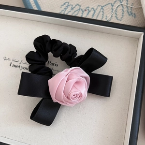 Pink satin rose and black bow scrunchie for women presented on a minimalist tray