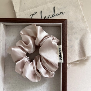 Macro detail of champagne satin scrunchie with silky texture and brand woven label