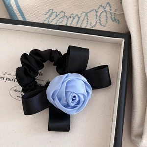 Detail view of a handmade pink satin scrunchie with blue rose and elegant bow accessory