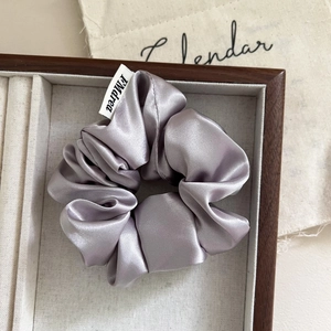 Elegant purple satin scrunchie with silky shine and brand label on a wooden tray
