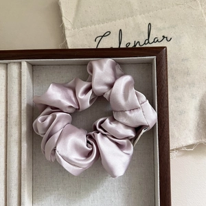 Detail of lilac satin scrunchie with silky folds on a wooden display tray