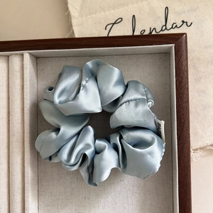 Light blue satin scrunchie with silky texture placed in a wooden jewelry box