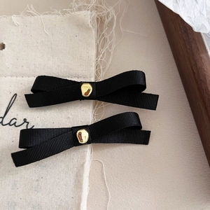 Close-up of black ribbon bow hair clips with gold metal accents on beige canvas