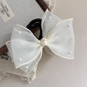Detailed shot of beige mesh bow hair claw clip with pearls on a textured background