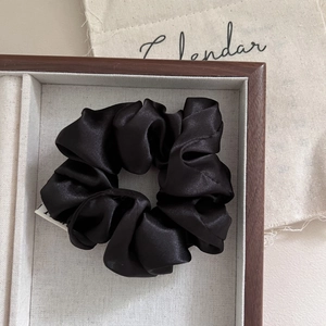 Detail of a black satin scrunchie with silk texture and white woven label on a wooden tray