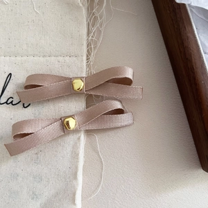 Detailed macro view of pair champagne gold ribbon bow hair clips with central gold buttons