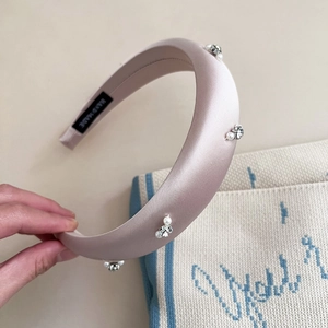 Pink satin padded headband with pearls and rhinestones shown in a hand-held detail view