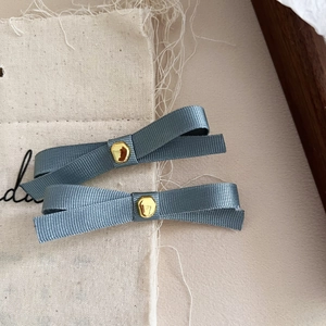 Close-up of grey blue ribbon bow hair clips with gold metal accents on fabric surface
