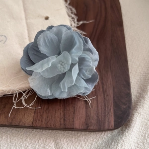 Dettaglio del fiore in tessuto chiffon blu Morandi su legno di noce e juta grezza