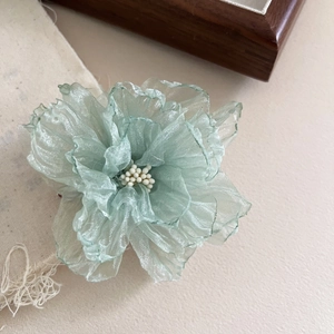 Vue macro détaillée d'une pince à cheveux fleur en organza vert clair avec perles blanches