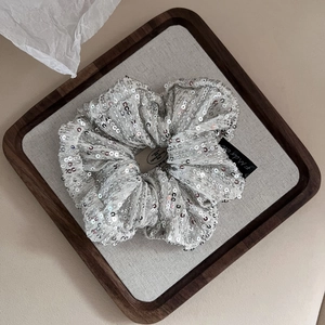 Elegant silver sequin scrunchie with handmade jewelry tag on a rustic wooden tray