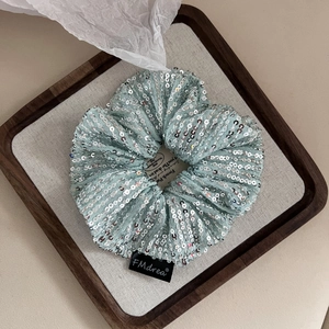 Close-up of mint green sequin scrunchie with silver sparkles on a wooden display tray