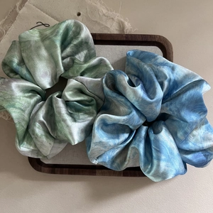 Detailed top view of teal and sky blue marble pattern satin scrunchies on a wooden tray