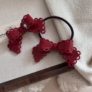 Deep red hollow bow hair clip and elastic tie set on rustic textured background