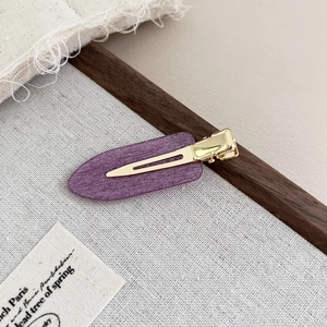 Detail view of purple acetate duckbill hair clip with brushed texture on linen fabric