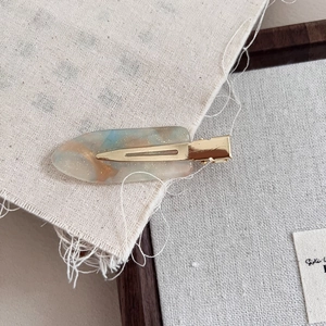 Detailed close-up of a blue and amber acetate hair clip with gold glitter and metal base