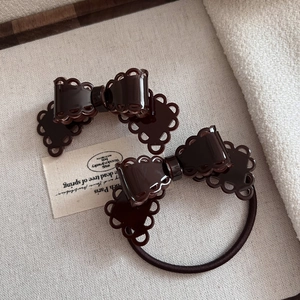 Detail of a dark brown acetate hair clip and elastic tie set with lace bow design