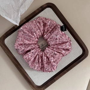 Detail of light pink sequin scrunchie hair tie with sparkling texture and brand tag