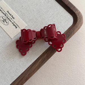 Detailed view of a red acetate bow hair clip with lace-style hollowed edges and glossy finish