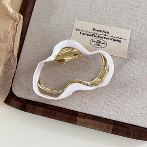 Detailansicht der unregelmäßigen Haarklammer mit weißer Emaille und Gold-Finish auf Stoff