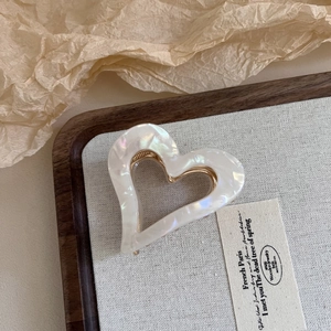 Detailed side view of a pearlescent white acetate heart claw clip with gold metal frame