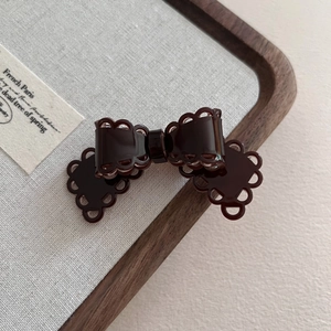 Close-up of a dark brown acetate bow hair clip with lace edges on a rustic wooden tray