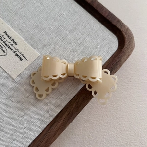 Close-up of cream acetate bow hair clip with hollow lace edges on a display tray