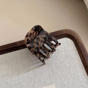 Detailed macro shot of elegant leopard print hair claw clip on a stylish wooden tray
