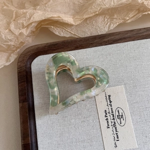 Marbled green heart-shaped hair claw clip made of acetate on a wooden display tray