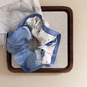 Detail of light blue and beige scrunchie with ink calligraphy print in a wooden tray