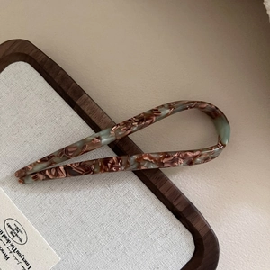 Detail der Acetat U-Haarnadel mit Marmormuster auf elegantem minimalistischem Holztablett