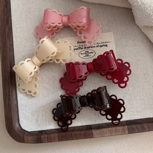 Elegant acetate lace bow hair clips in four colors on a textured cream fabric tray