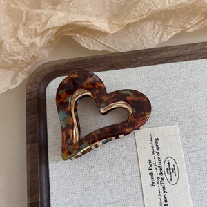 Elegant tortoiseshell acetate heart hair claw clip with golden spring on wooden tray