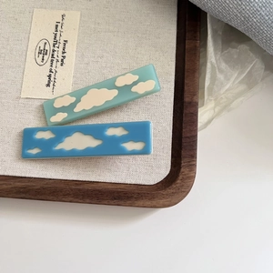 Chic acetate hair clips with blue cloud patterns on a rustic wooden display tray