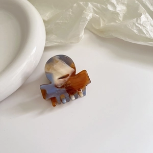 Detailed shot of tortoiseshell acetate hair claw with gold logo on elegant ceramic plate