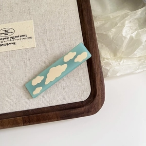 Chic acetate hair clip with sky blue finish and white cloud pattern on wood tray