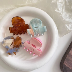Set of four mini acetate hair claws in amber, mint, and pink marble patterns on white plate