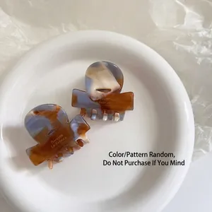 Elegant amber and blue marble acetate hair claw clips in a white ceramic dish