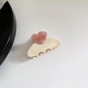 Detail of a cream hair claw clip with a pink marble textured heart on a white background
