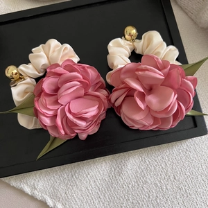 Detailed macro view of 3D satin camellia scrunchie with silk leaves and golden bead accent