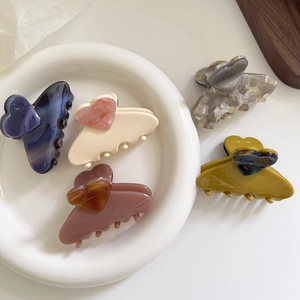 Set of five heart-shaped acetate hair claws in various colors on white ceramic tray