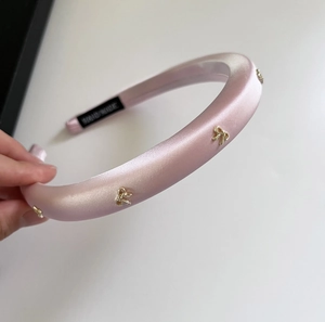 Dettaglio del cerchietto in raso rosa imbottito con piccoli fiocchi dorati decorati