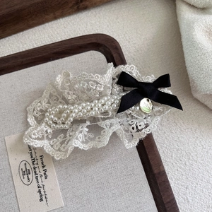 Close-up of beige lace hair clip with pearls and a small black ribbon bow detail