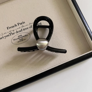Pince à cheveux noire minimaliste avec perle en métal argenté sur un plateau en tissu